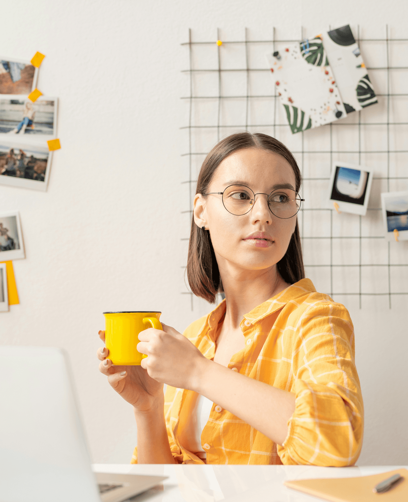 Woman with glasses holding yellow mug at desk