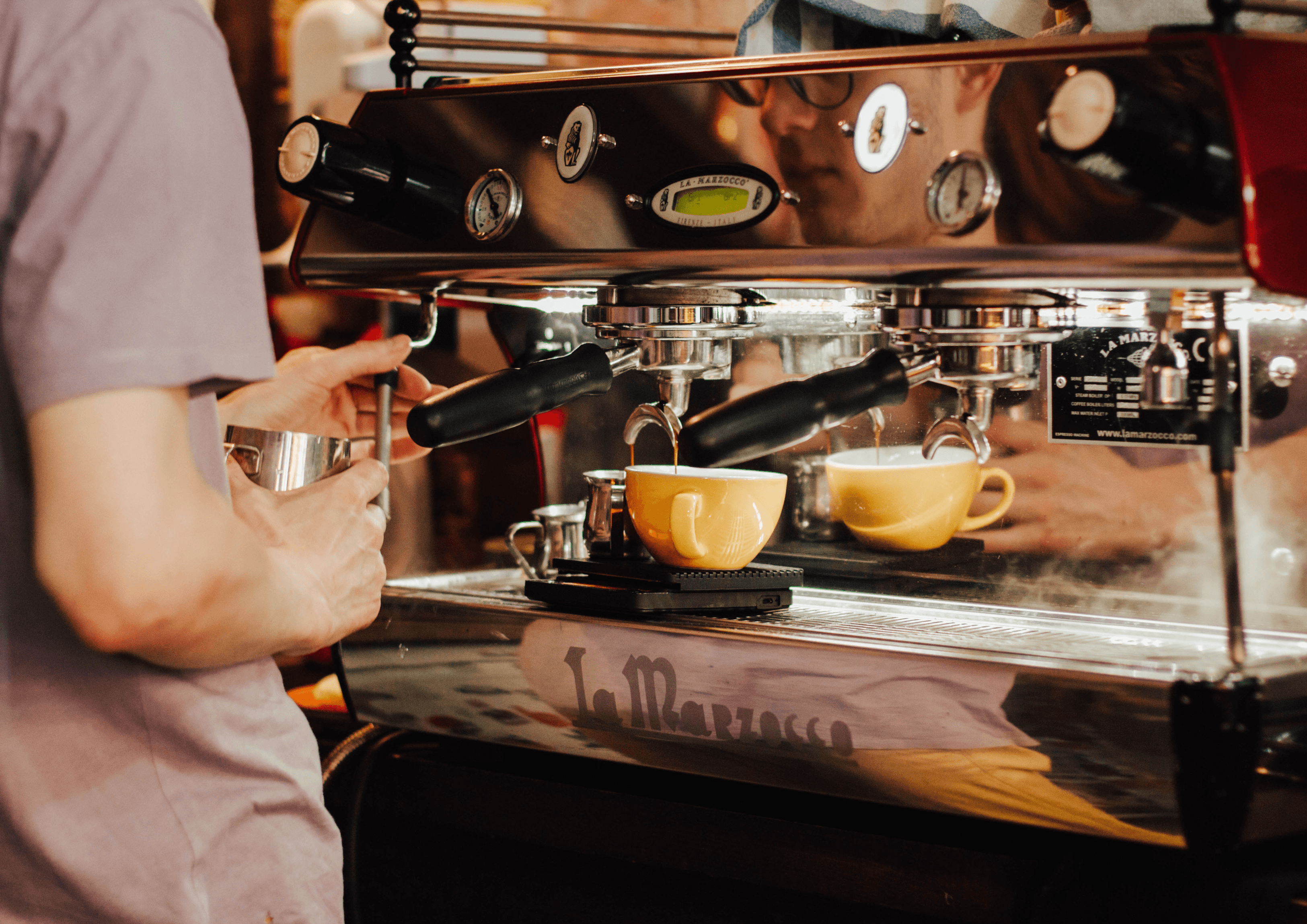 A cafe owner is making coffees for their customers
