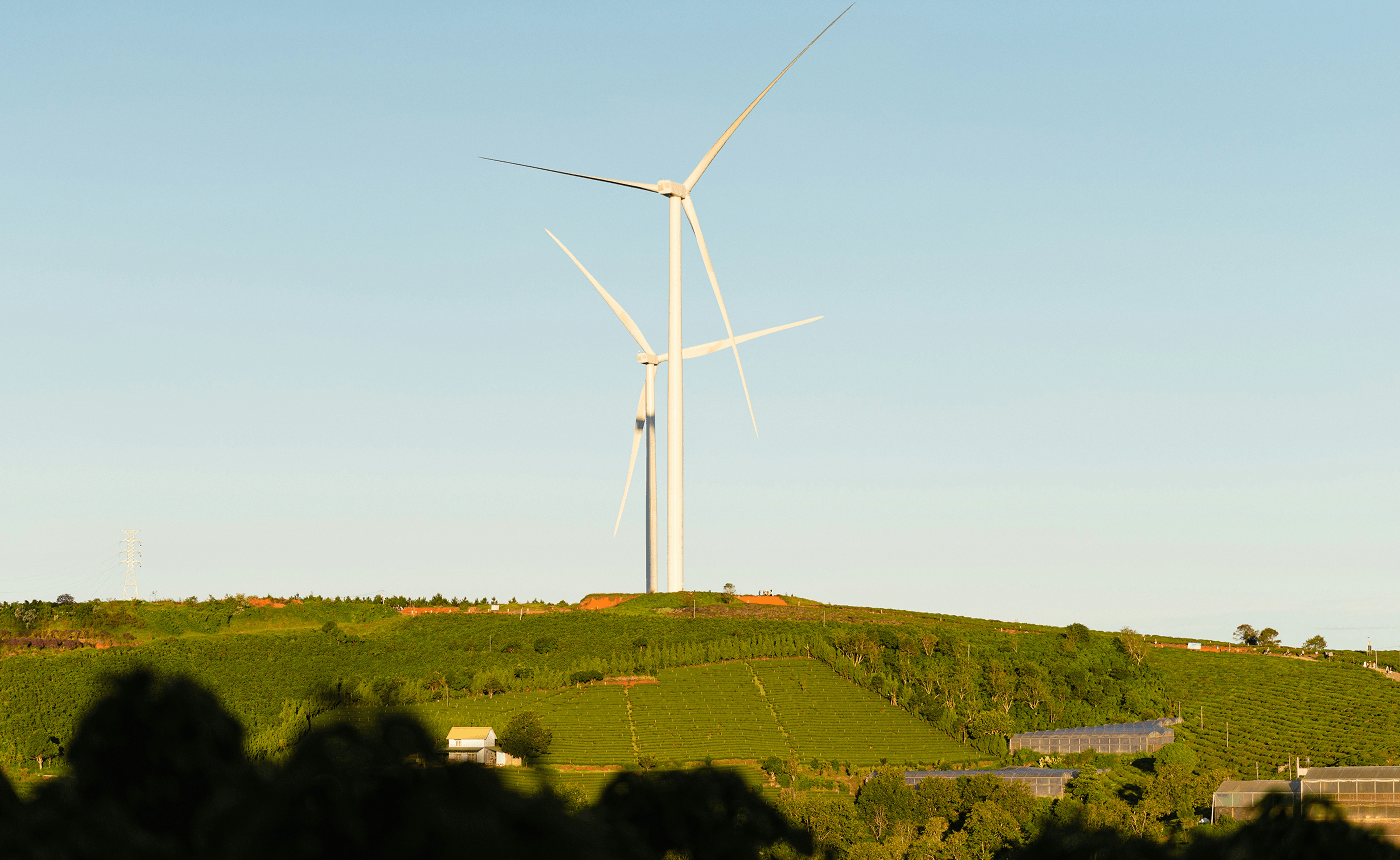 A wind turbine stands on a grassy hill under a clear blue sky